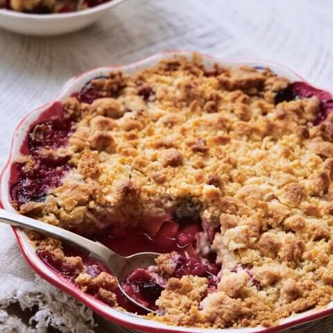 A rhubarb crumble with one serving in a white bowl on white linen