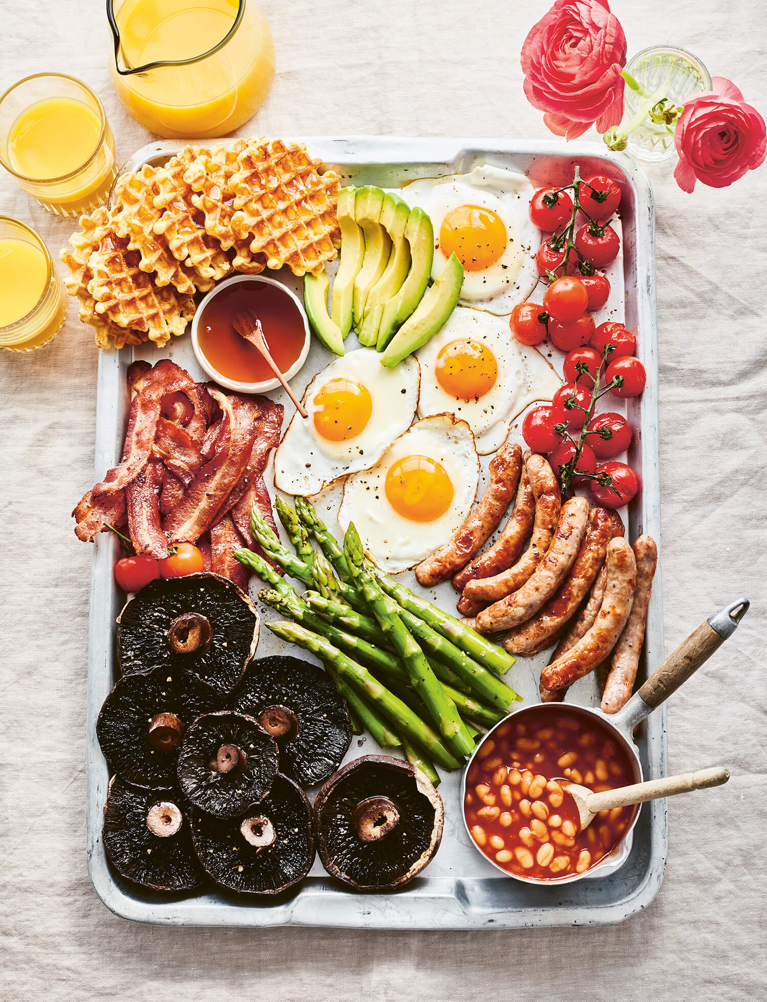 A baking sheet laid with traditional breakfast items on a white tablecloth with glasses of juice