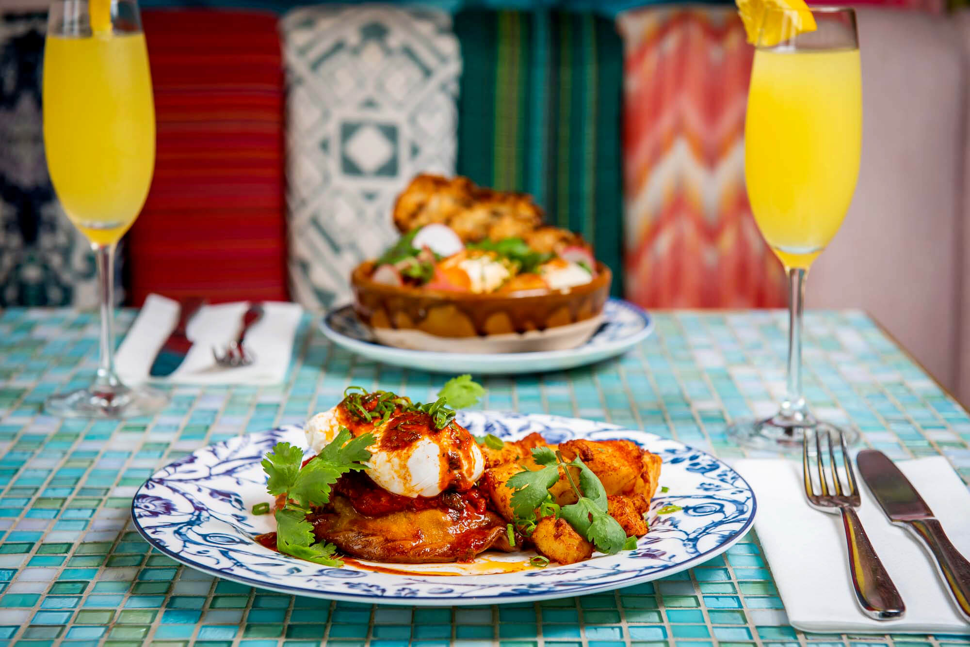 Two plates with empanadas and mimosas on a colourful table.