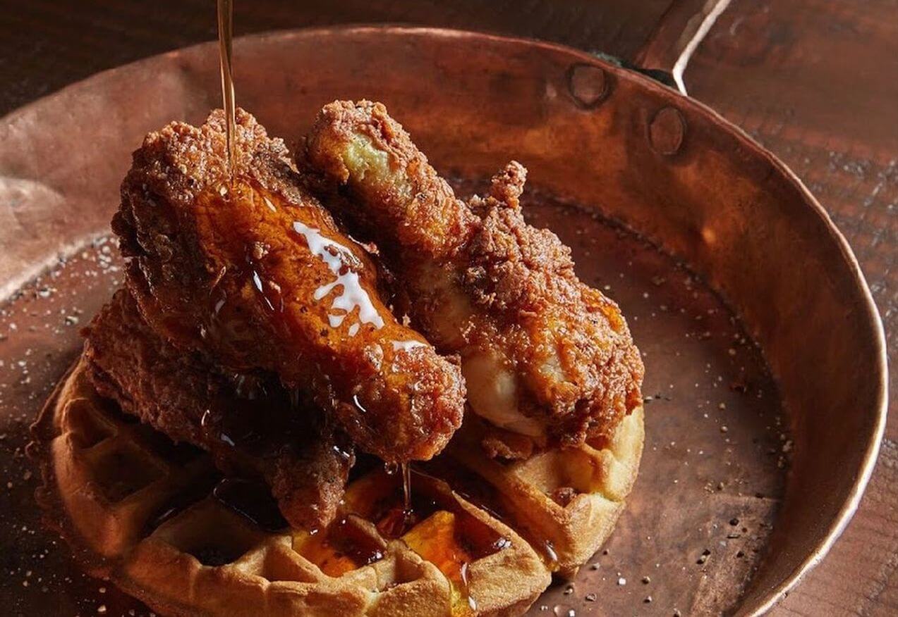 Syrup being poured over waffles and chicken