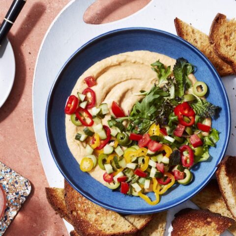 Bowl of creamy vegan navy bean dip with layers of chopped veggies and herbs