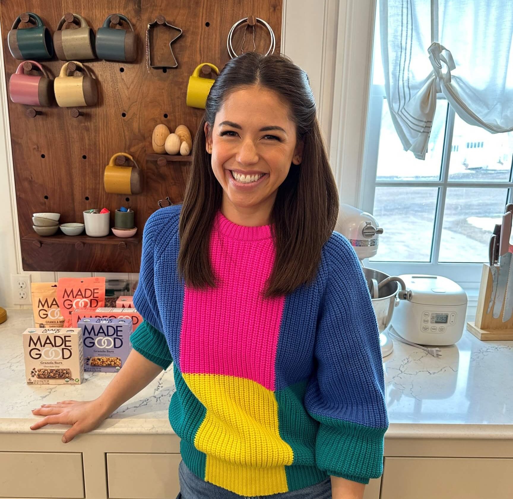 A woman, Molly Yeh, smiles in front of a countertop with a bright sweater on.