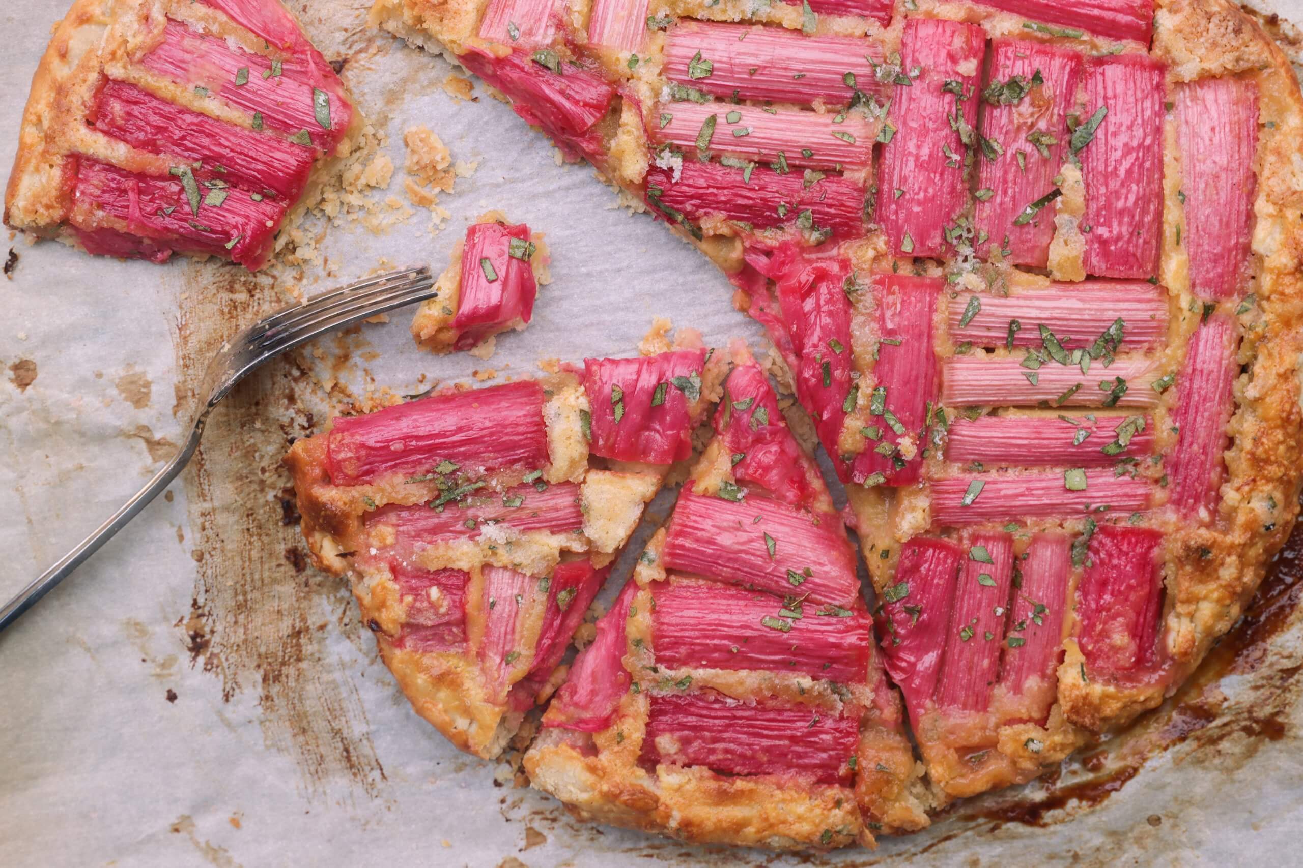 A galette with pieces of rhubarb on top, sliced into pieces with a fork visible.