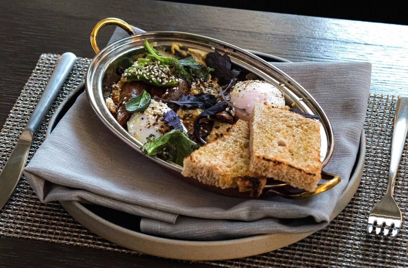 A silver serving tray with toast, sausages and eggs and greens