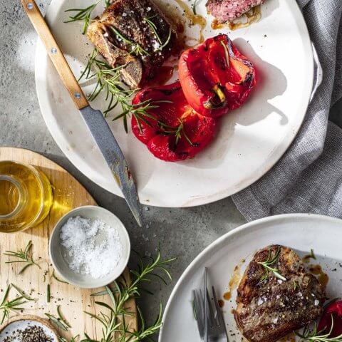White plates with grilled lamb chops, red peppers and herbs