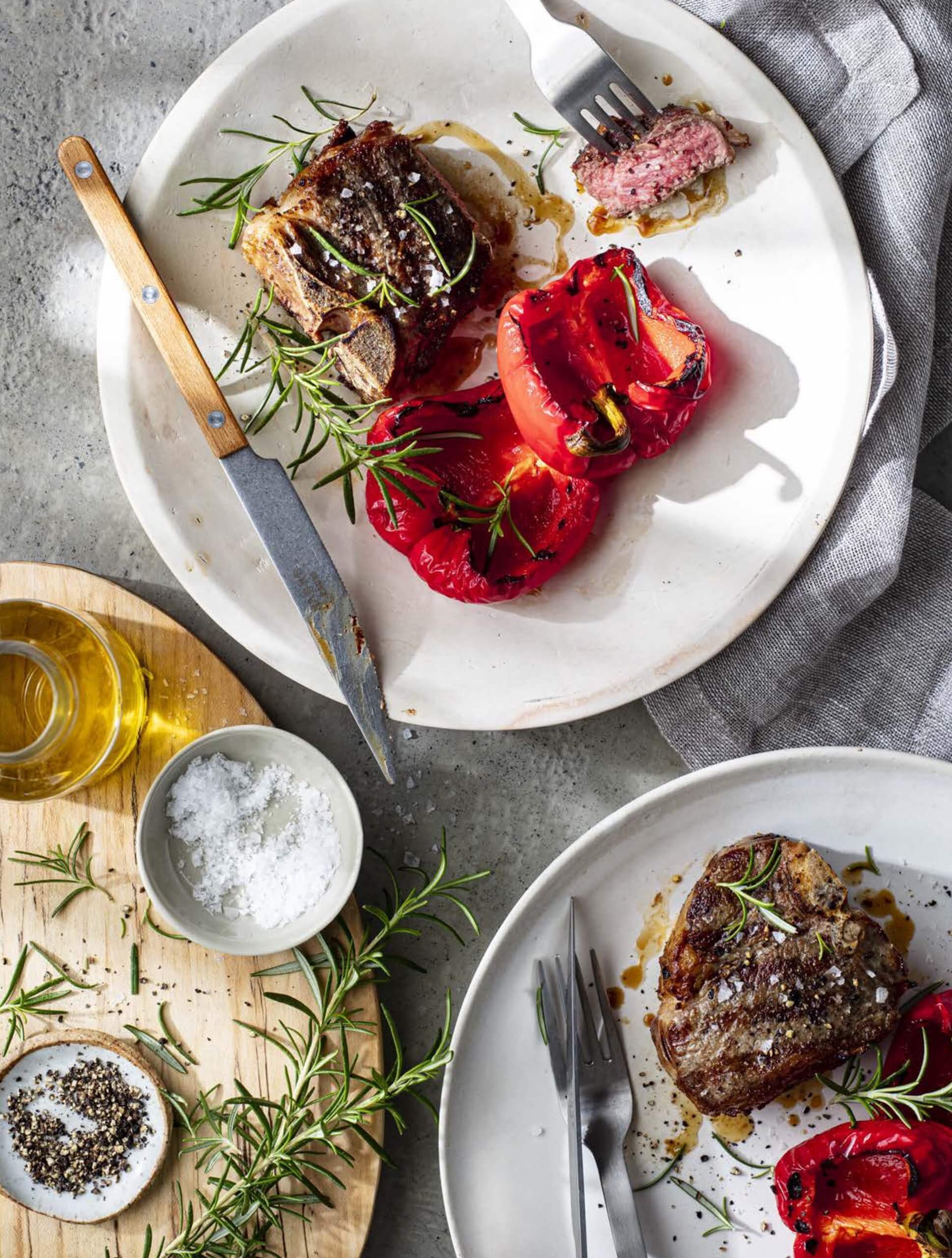 White plates with grilled lamb chops, red peppers and herbs