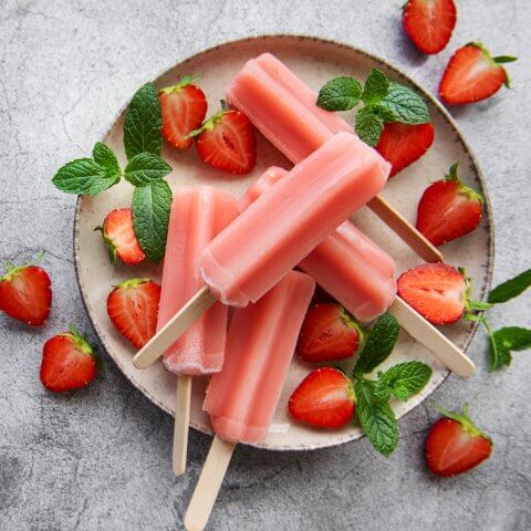 A plate of popsicles surrounded by strawberries and green garnishes