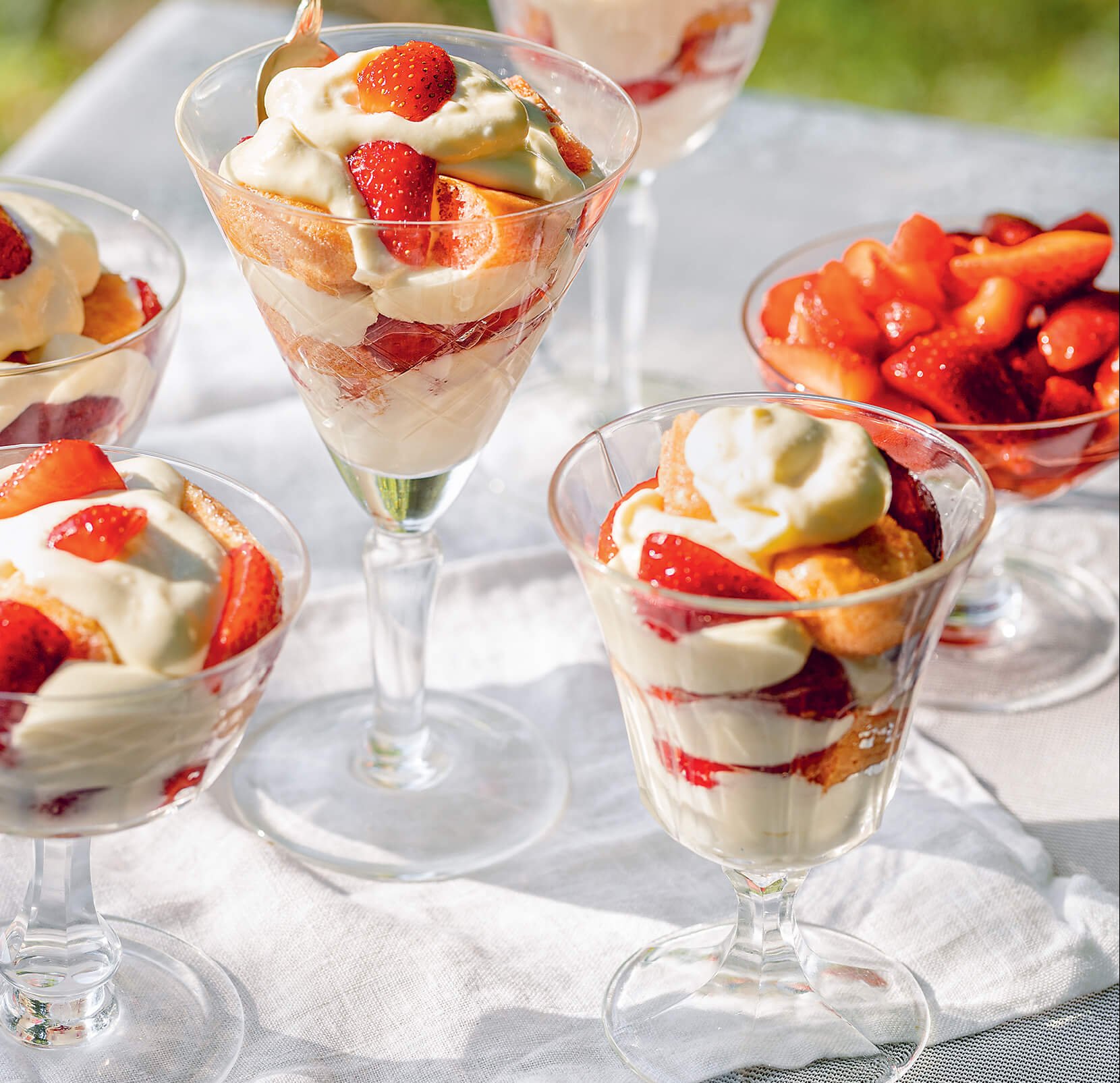 A white cloth on grass laid with strawberry parfaits
