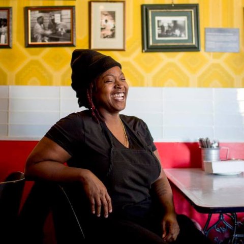 A woman sitting at a table in a dining room with yellow walls covered in photos.