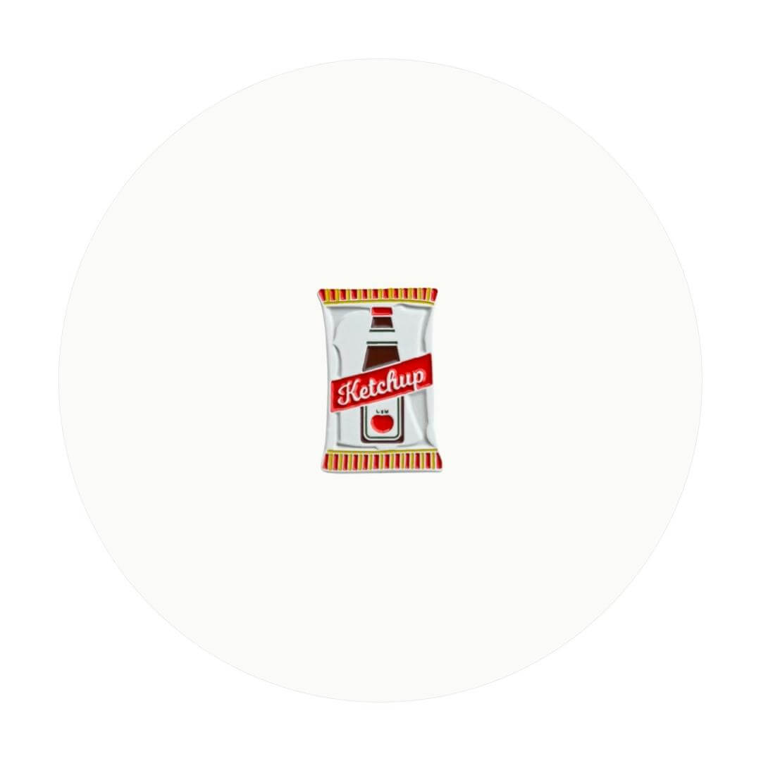An enamel pin modelled after a bag of ketchup chips on an off-white circle graphic