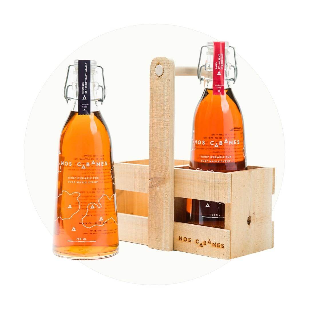 Two bottles of maple syrup and a wooden carrying case on an off-white circle graphic.