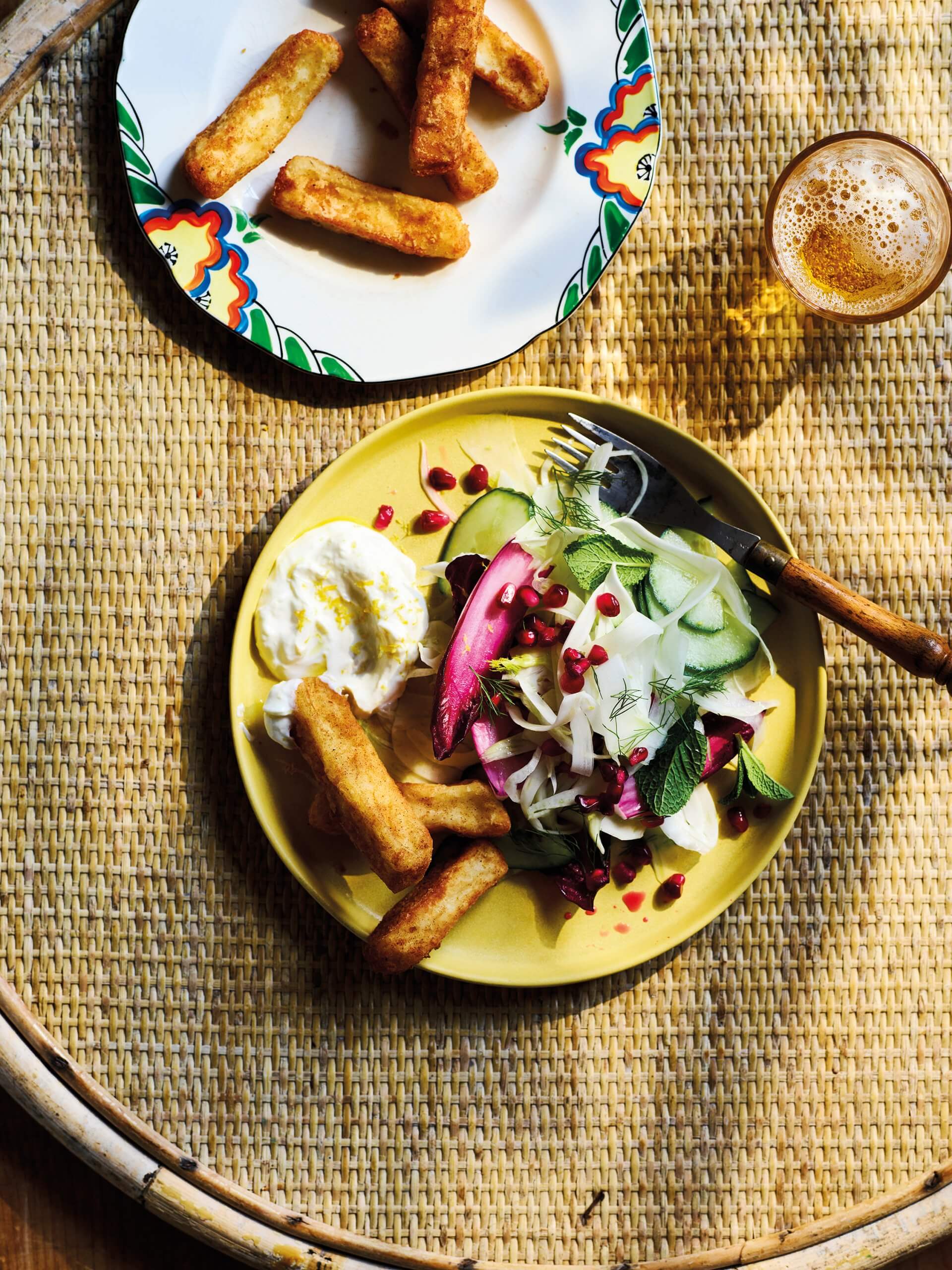 A yellow plate with salad and potato wedges on a woven yellow table surface