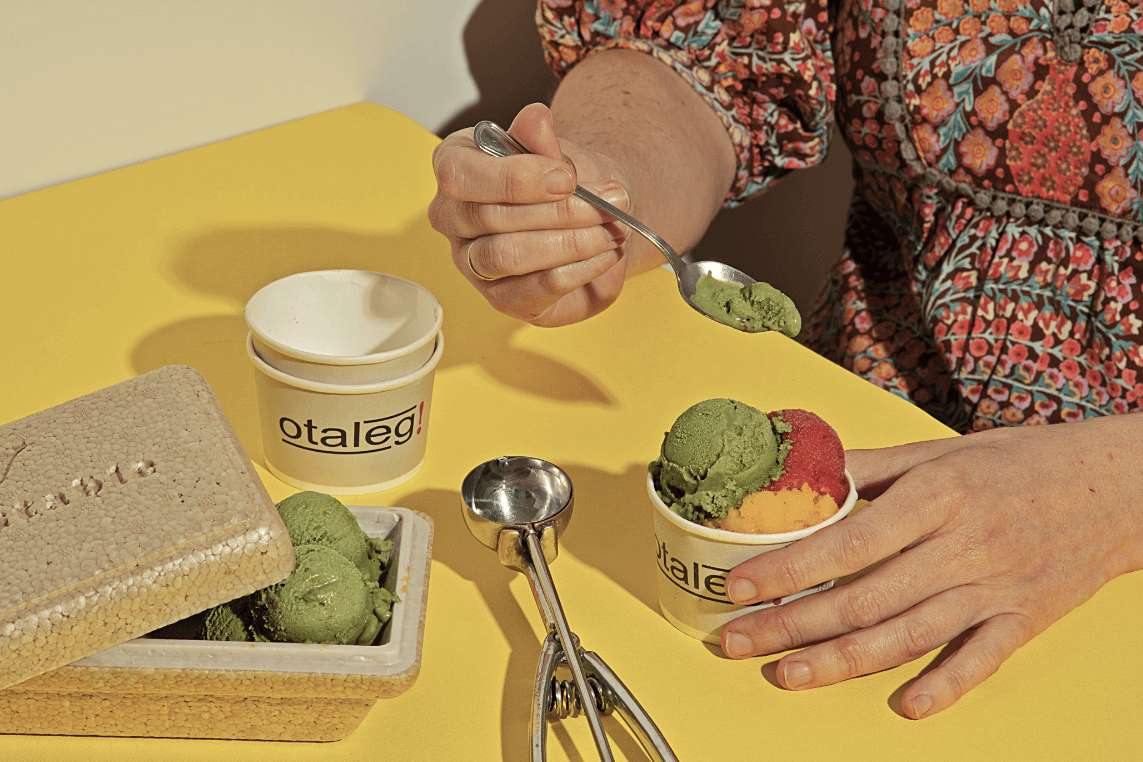 A person eating gelato from a paper cup on a bright yellow tabletop