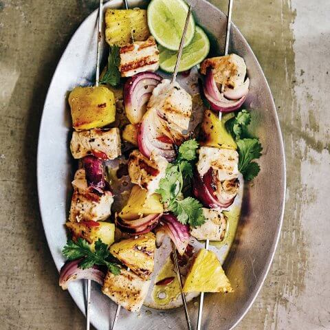 A plate with metal skewers with grilled fish and pineapple