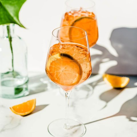Two orange spritz cocktails with orange wheels on a stark white and sunny backdrop