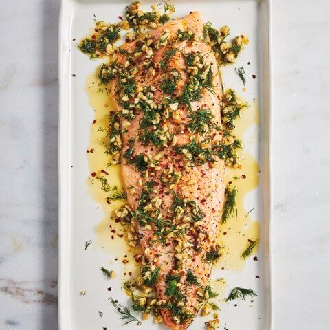 Fish covered with herbs and oil on a white plate on a marble countertop