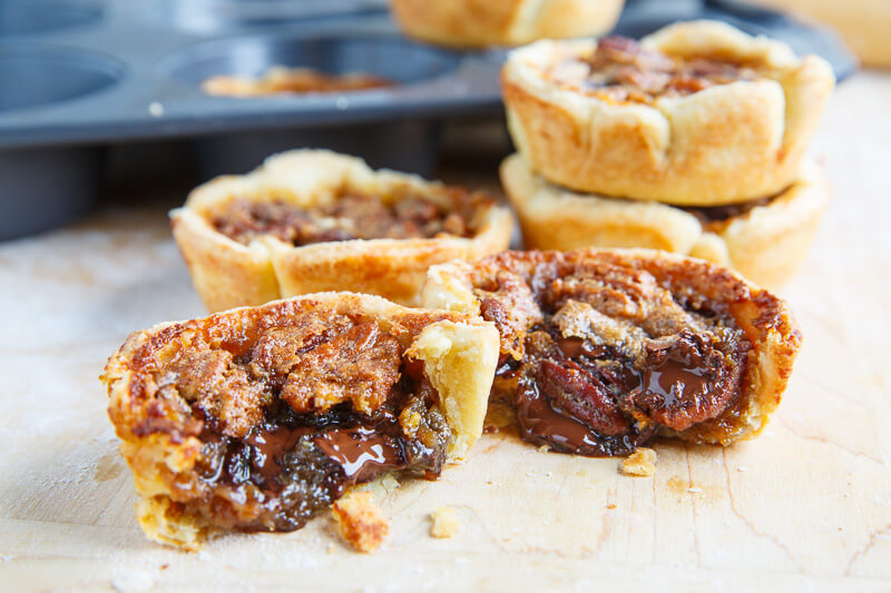 A butter tart broken in half to show a chocolate centre, with more tarts and a baking pan visible in the background