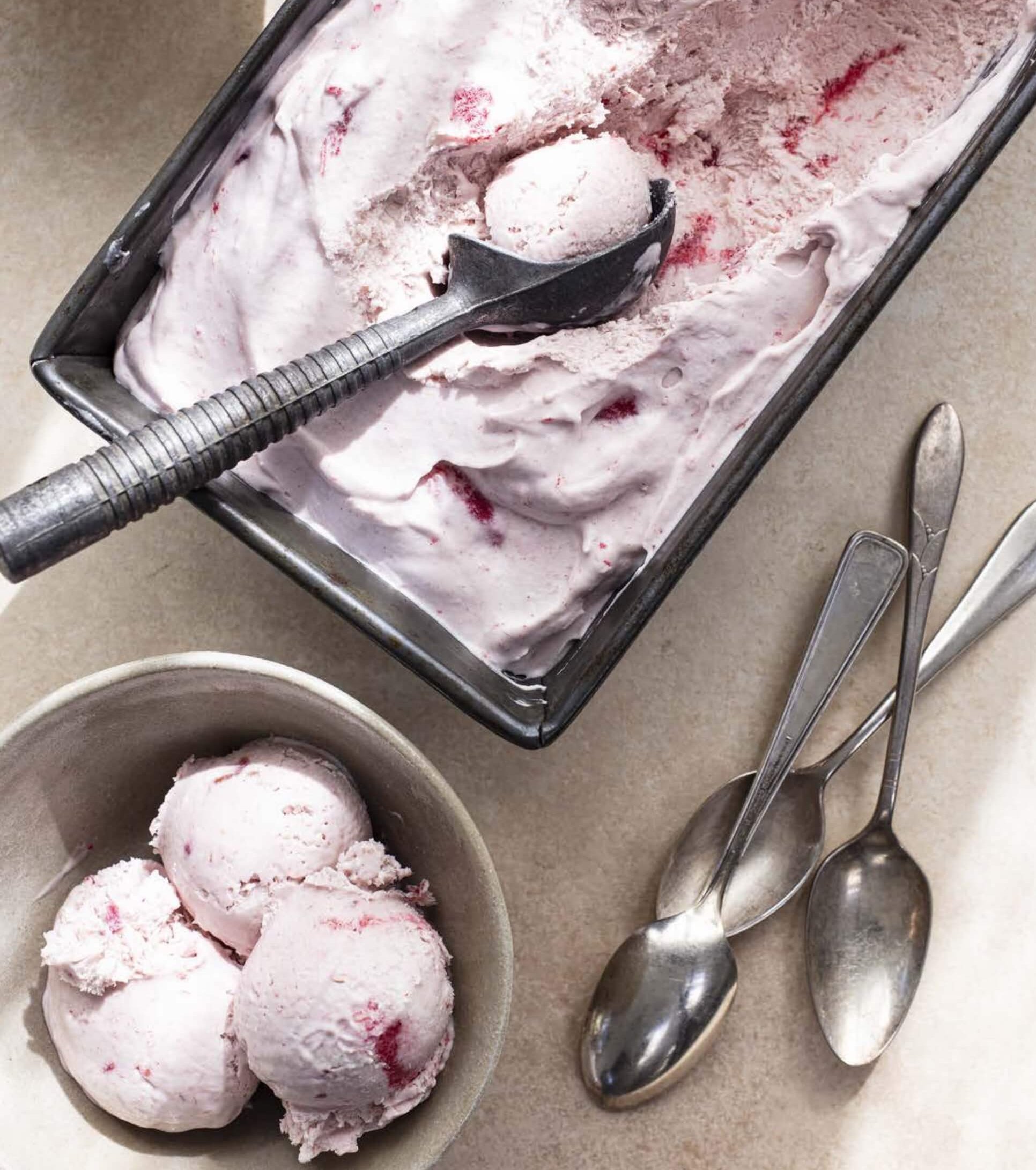 A pink-coloured ice cream in a silver vat with scoops and spoons