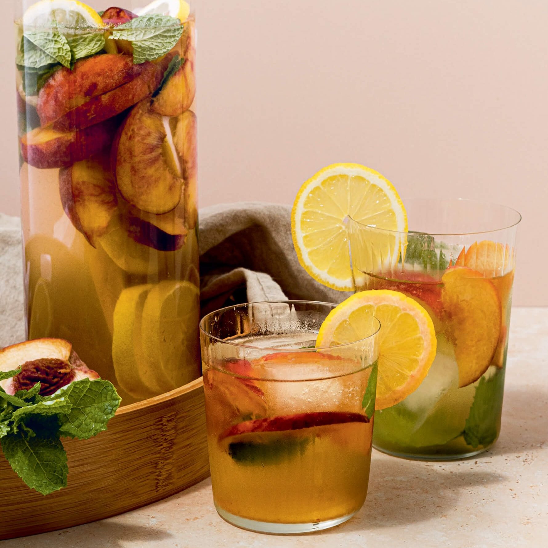 A pitcher and glasses of sangria filled with fresh fruit on a surface against a light pink background