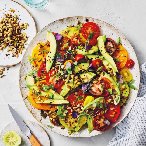 A white plate with an avocado, tomato and grain salad
