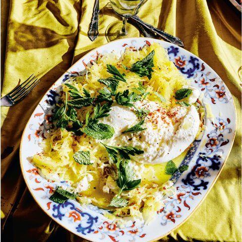 A plate with spaghetti squash and burrata on a silky yellow tablecloth