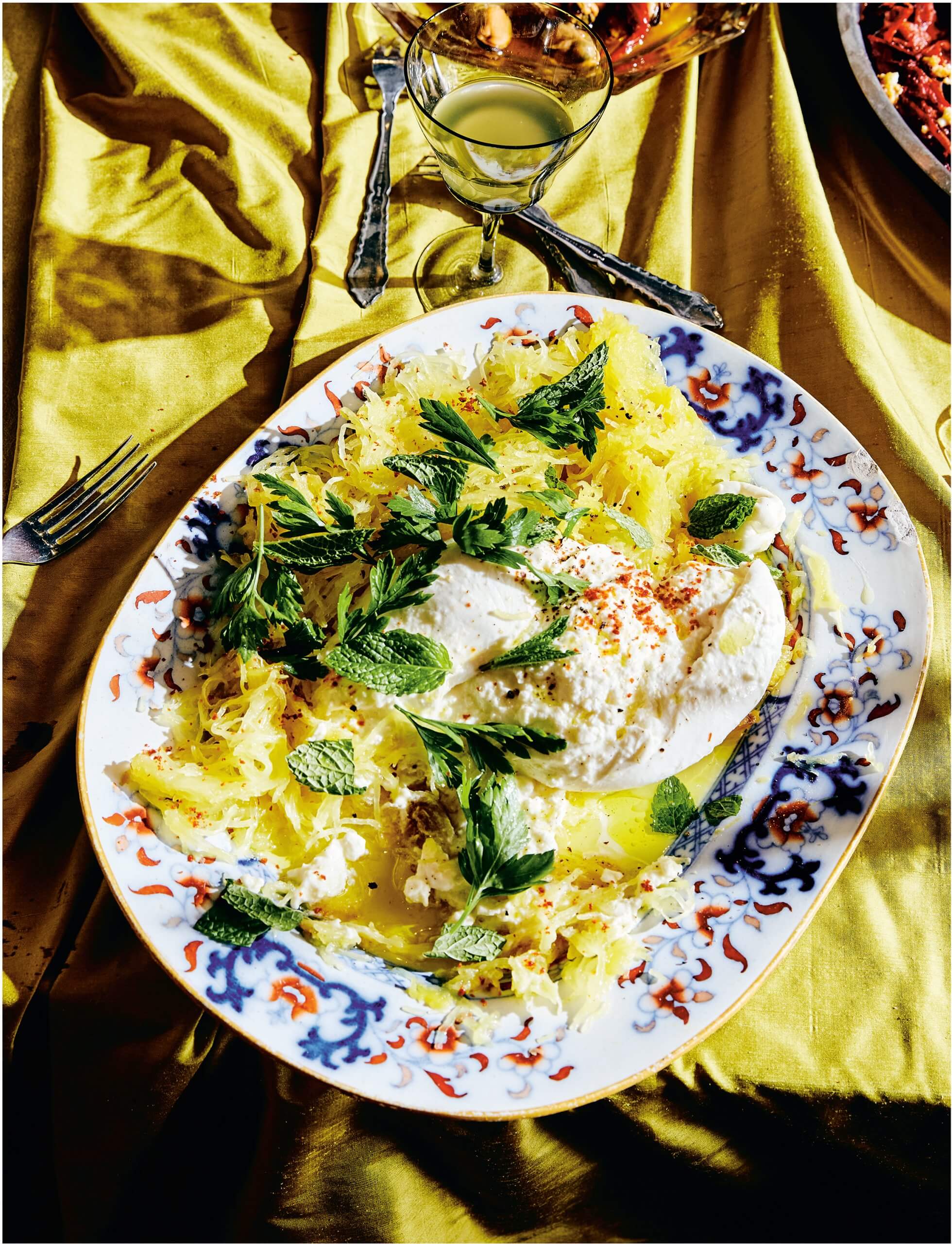 A plate with spaghetti squash and burrata on a silky yellow tablecloth