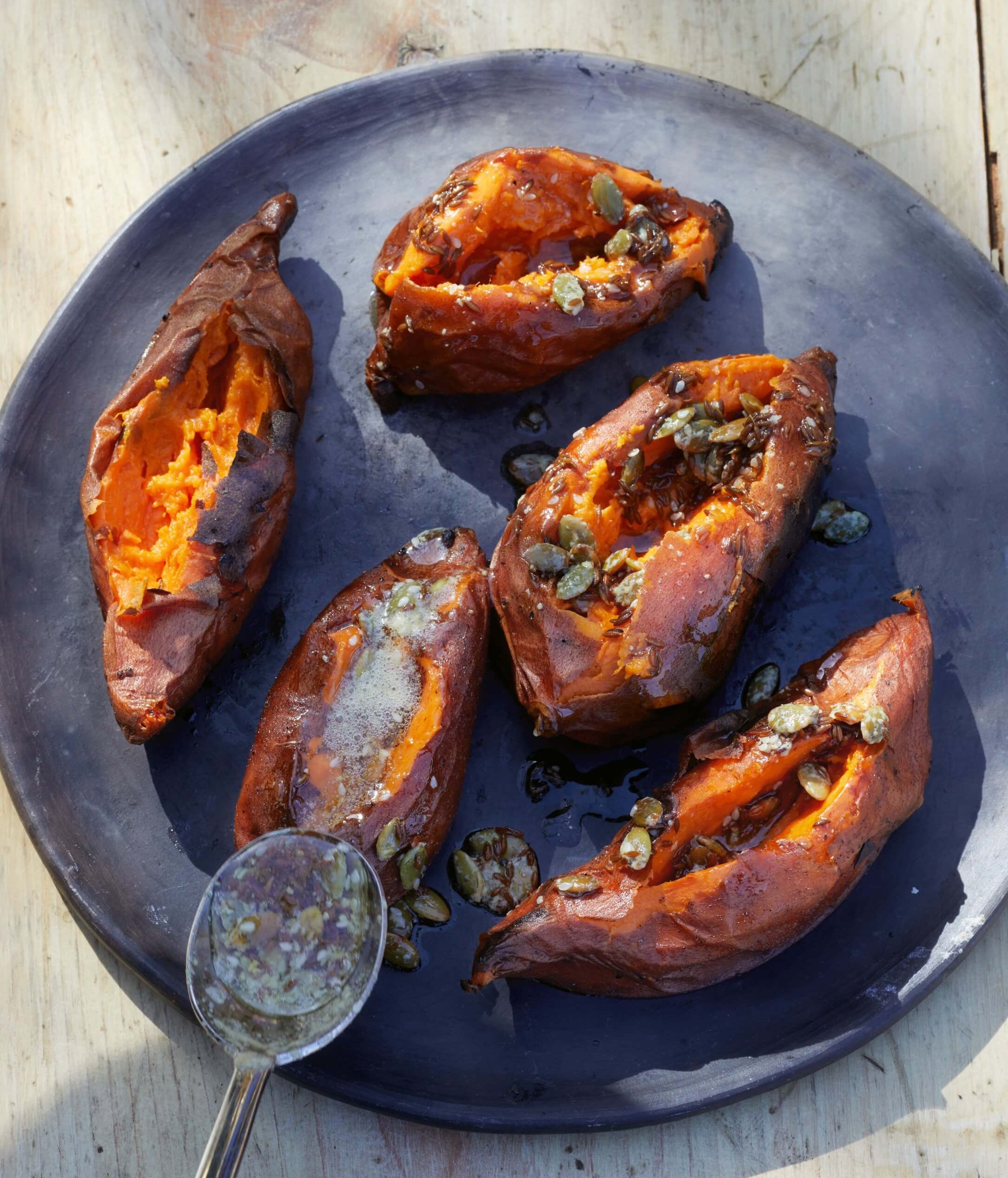 A dark blue dish with roasted sweet potatoes and a spoon visible