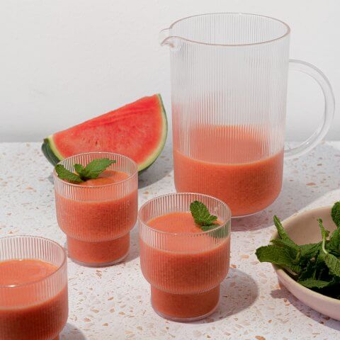 A pitcher of pink juice with some poured into glasses and a wedge of watermelon