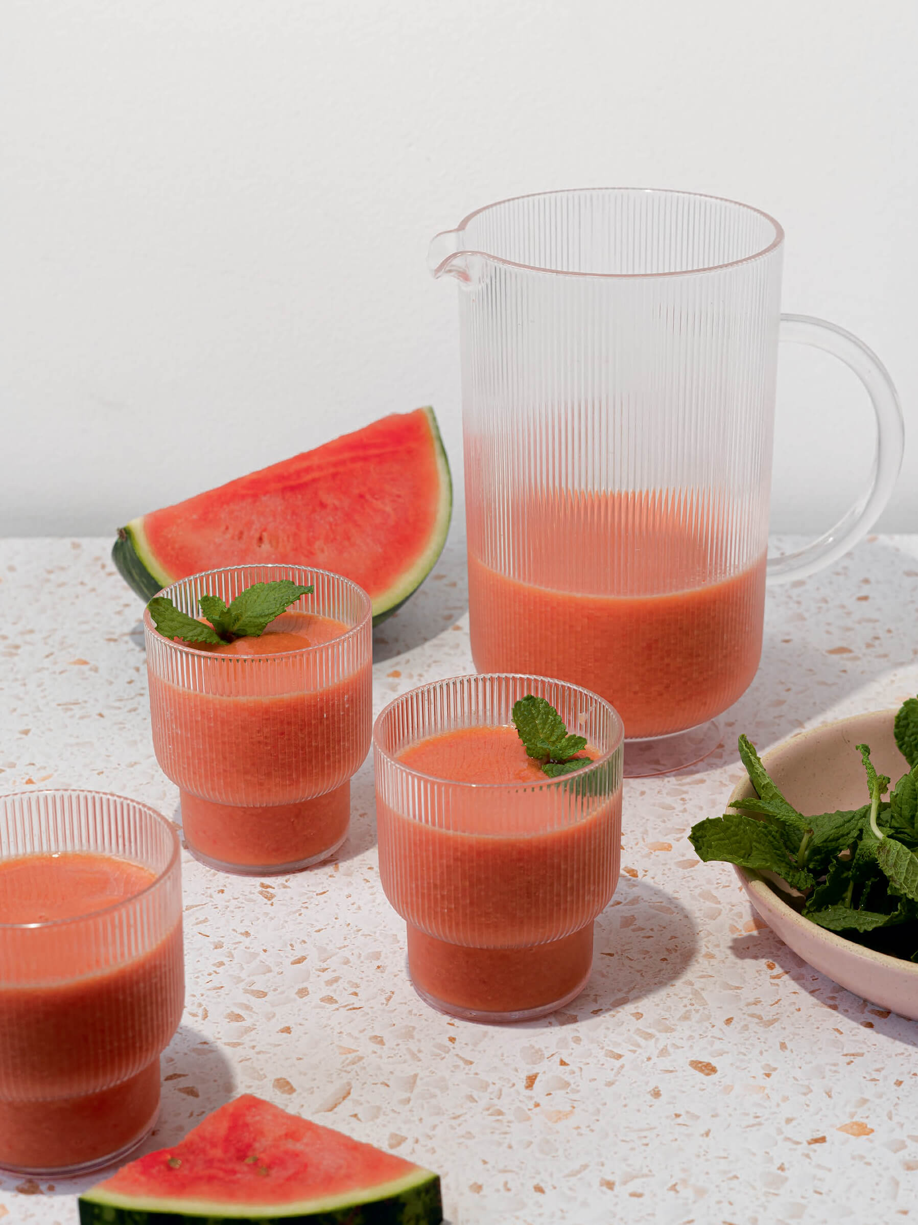 A pitcher of pink juice with some poured into glasses and a wedge of watermelon