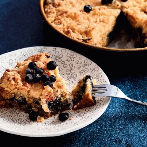 A slice of blueberry crumb cake on a white plate on a blue surface