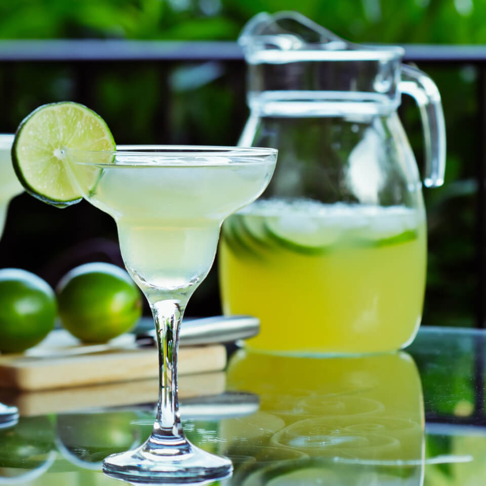 A margarita glass with a lime wheel and half-full pitcher visible in the background