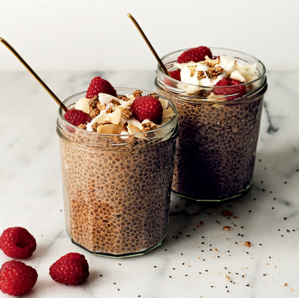 Two clear jars of chocolate chia pudding topped with berries on a marble surface