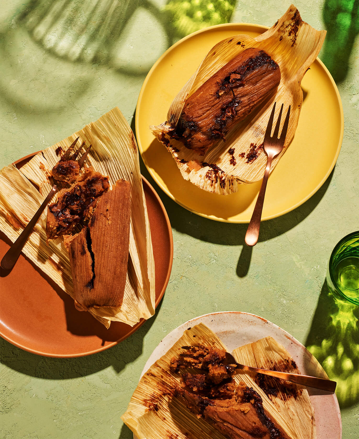 A yellow, brown and pink plate with chocolate tamales on a green table