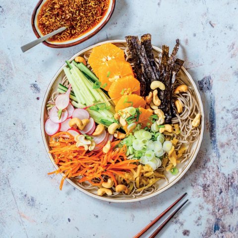 A bowl of salad with multicoloured ingredients, a dish of sauce and chopsticks