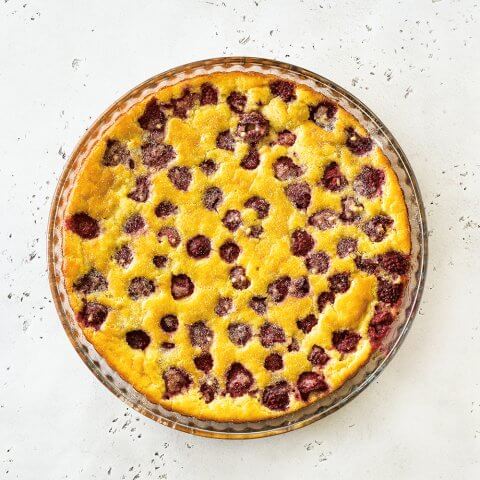 A yellow cake with raspberries on a white linoleum background