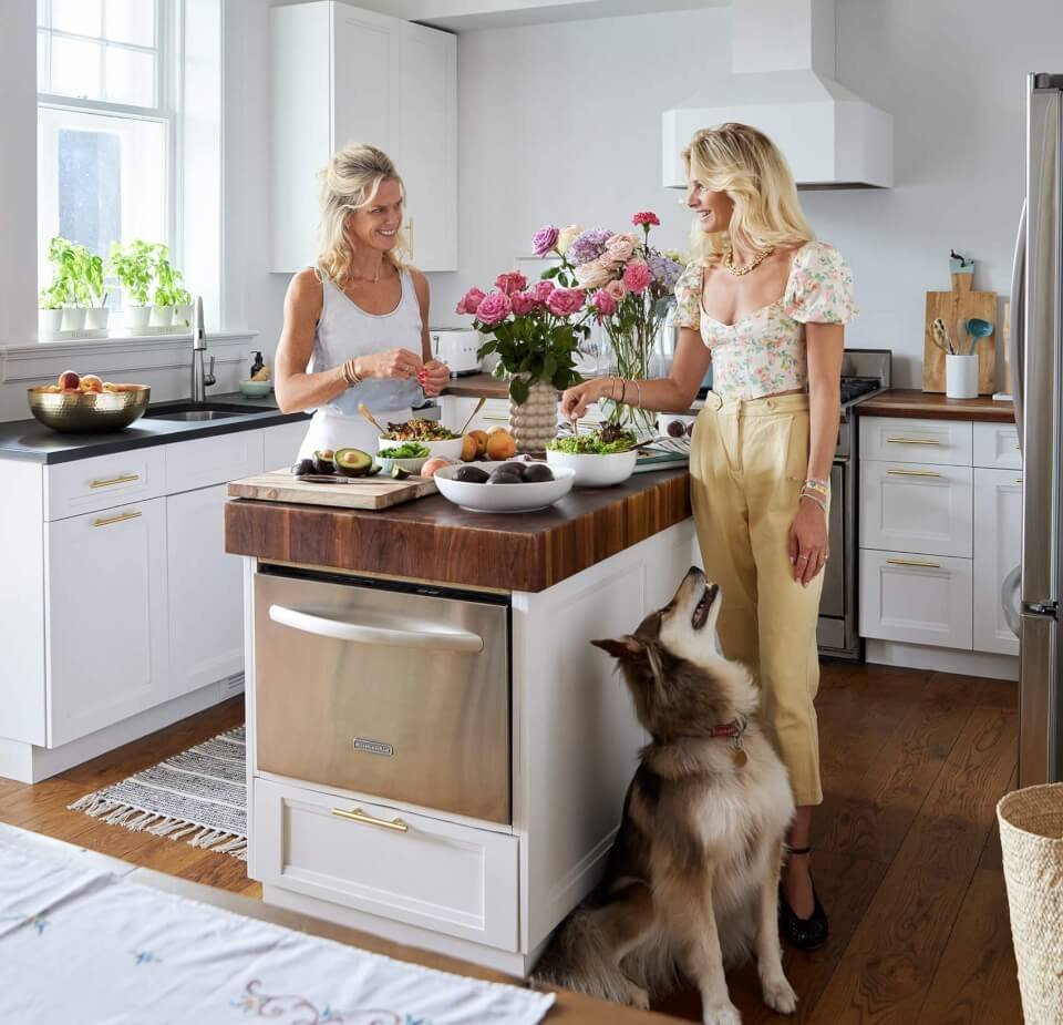 Two women and a dog standing on opposing sides of a kitchen island