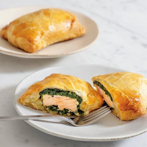 A pastry wellington stuffed with salmon and spinach on a white plate on a marble countertop