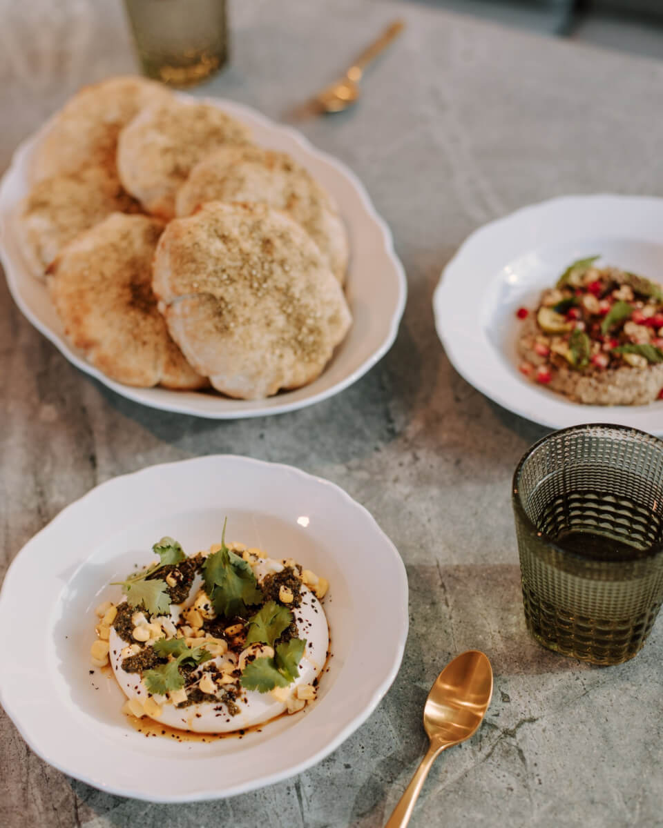 A table set with white dishes, gold silverware and green glassware