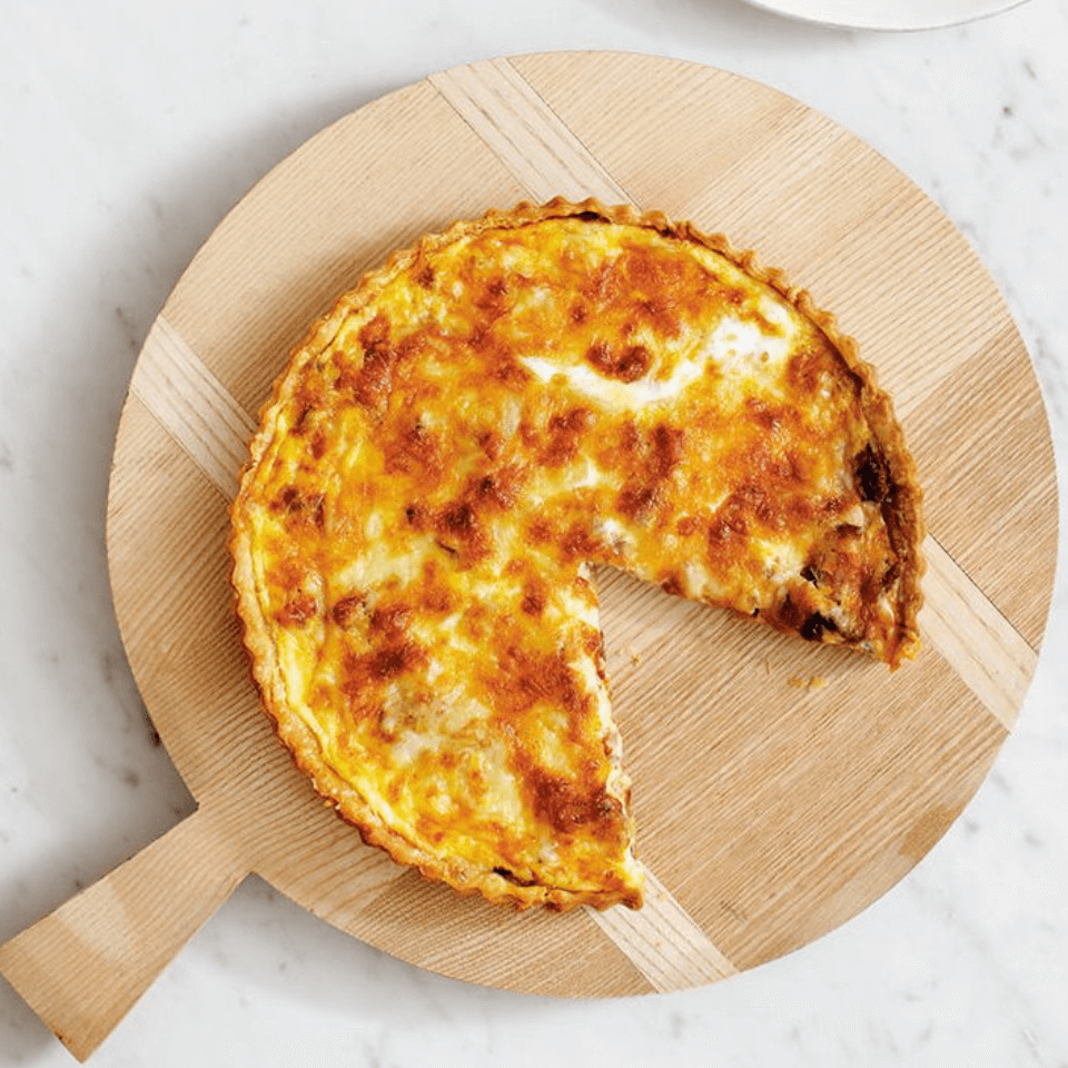 A quiche on a wooden tray with a slice on a white plate next to it