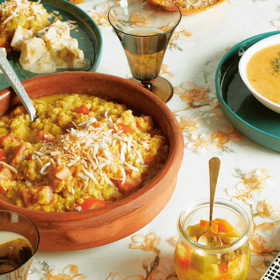 A table with a floral tablecloth and multicoloured dishes with rice and curry