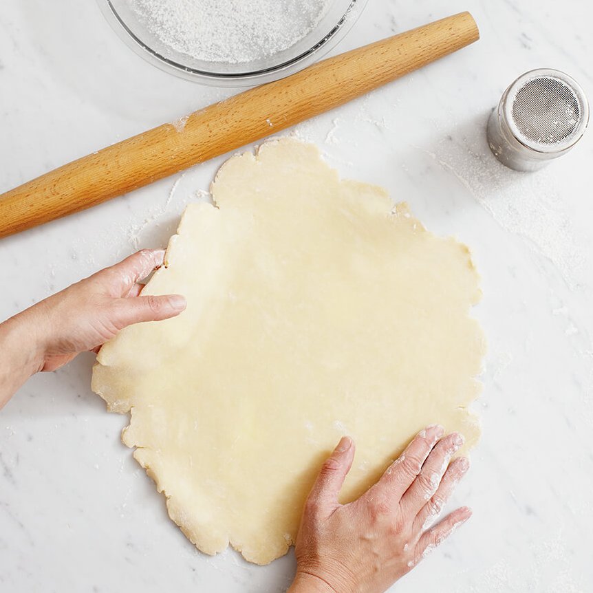 A person rolling out pie dough on a white marble surface
