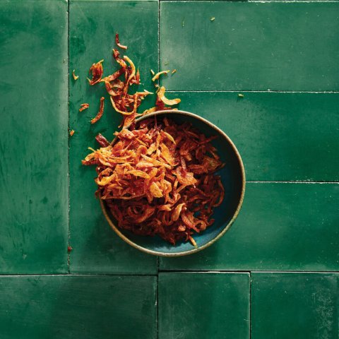 A bowl of fried shallots on a green tiled surface