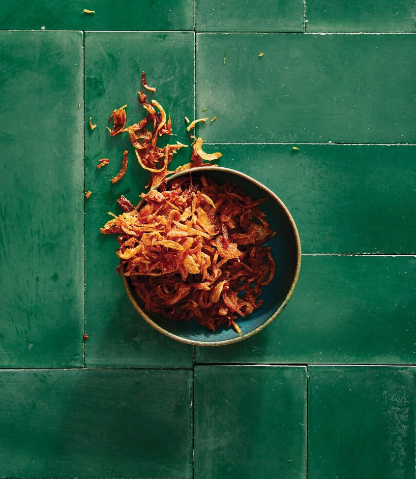 A bowl of fried shallots on a green tiled surface