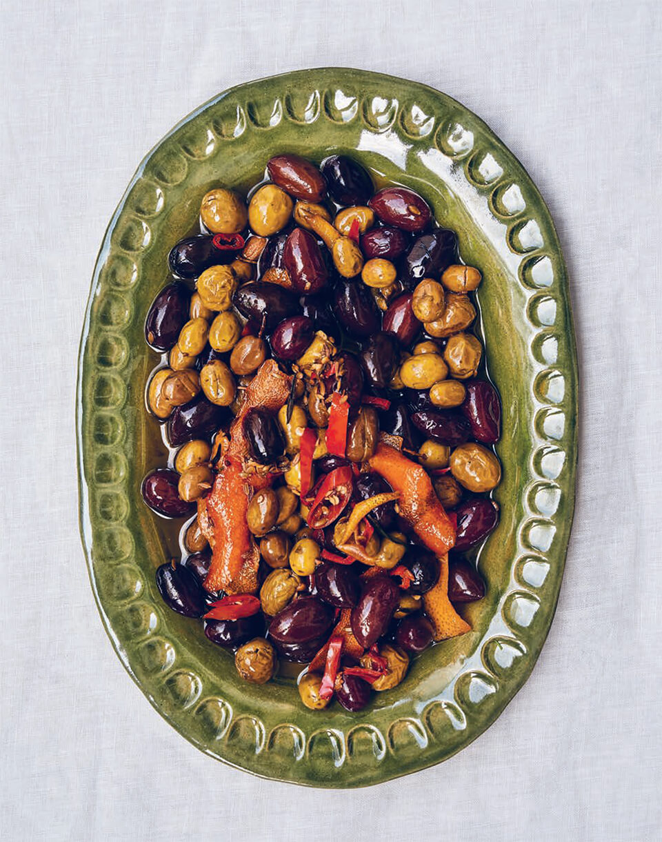A green dish with mixed olives on a white tablecloth
