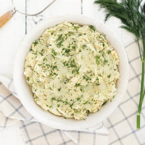 A white bowl of mashed potatoes with dill