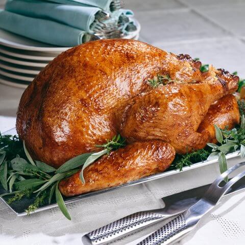 A turkey on a serving dish with plates and blue napkins in the background
