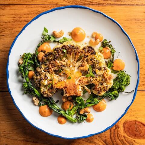 A dish with a roasted cauliflower steak, greens and orange sauce