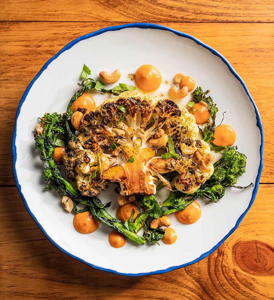A dish with a roasted cauliflower steak, greens and orange sauce