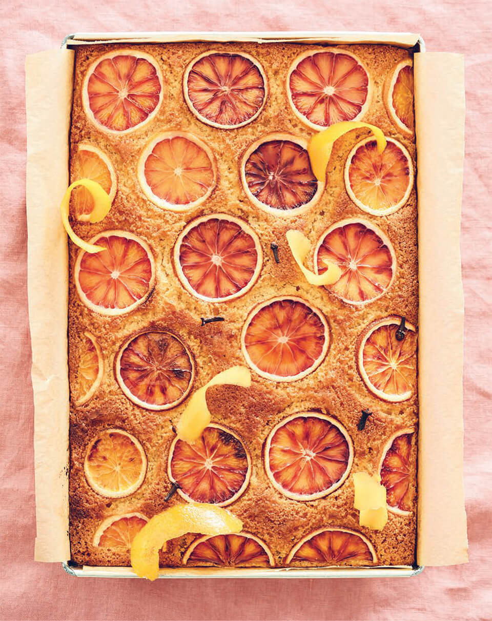 A semolina cake with citrus slices on top over a light pink bagkround