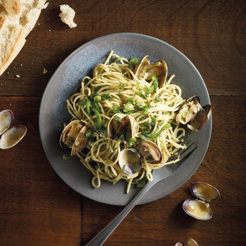 A dish of spaghetti with clams and a piece of bread on a dark wooden surface